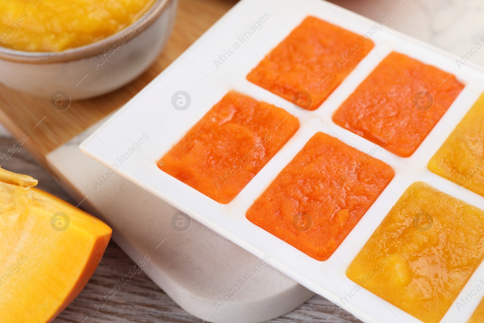 Photo of Different purees in ice cube tray ready for freezing on table, closeup