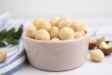 Photo of Tasty peeled Macadamia nuts in bowl on white table, closeup