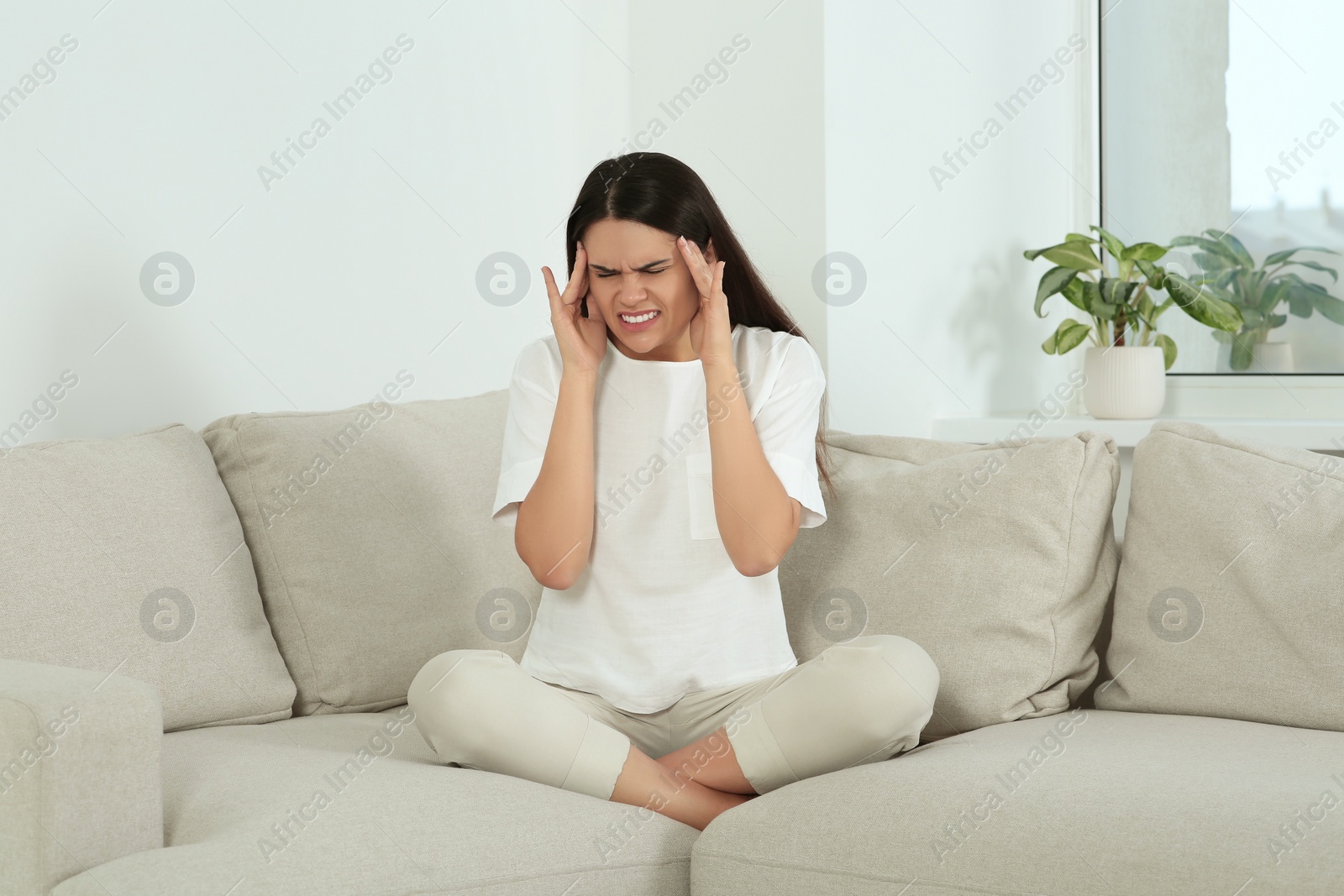 Photo of Young woman suffering from headache on sofa at home. Hormonal disorders