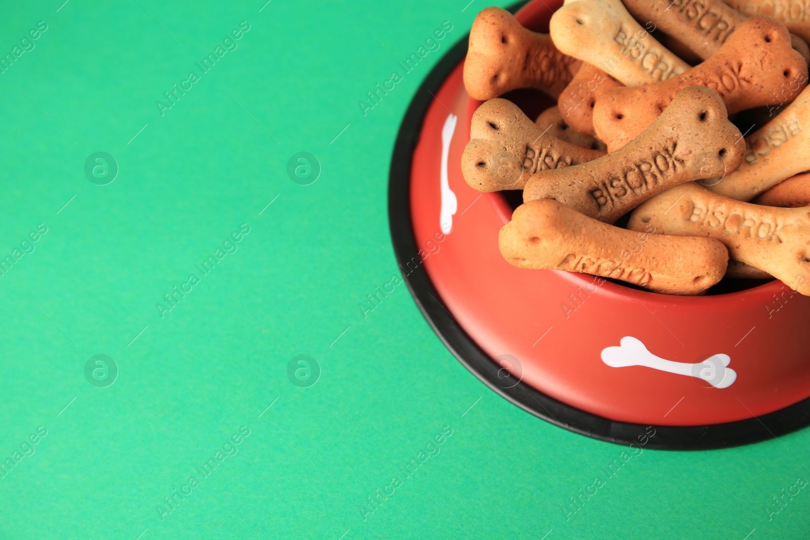 Photo of Bone shaped dog cookies in feeding bowl on green background, space for text
