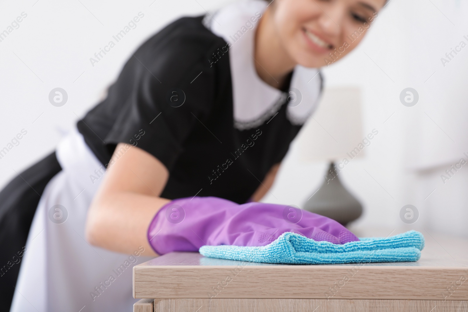 Photo of Young maid dusting furniture with rag in hotel room, closeup