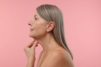 Beautiful woman touching her neck on pink background