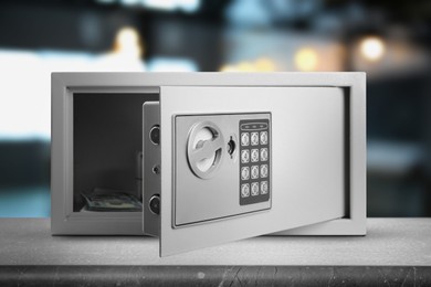 Open steel safe with electronic lock and money on grey table indoors