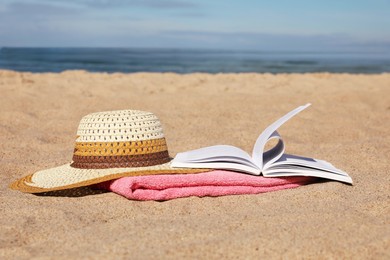 Photo of Open book, hat and pink towel on sandy beach near sea
