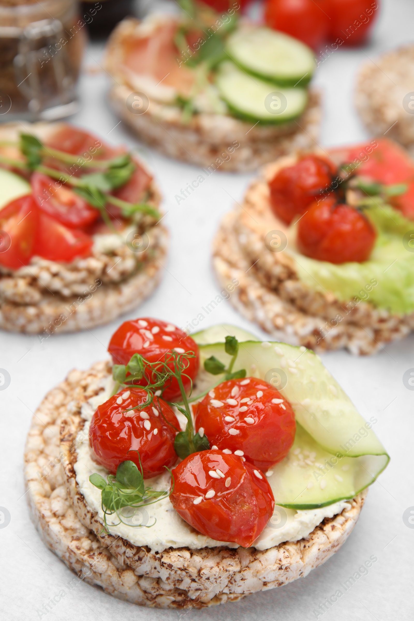 Photo of Crunchy buckwheat cakes with cream cheese, tomatoes and cucumber slices on white table, closeup