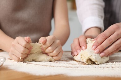 Photo of Making bread. Mother and her daughter kneading dough at wooden table indoors, closeup