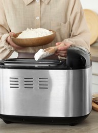 Photo of Making dough. Woman adding flour into breadmaker machine at wooden table, closeup