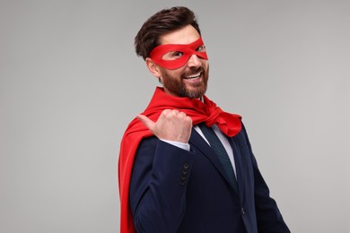 Photo of Happy businessman wearing red superhero cape and mask on beige background