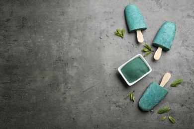 Photo of Flat lay composition with delicious spirulina popsicles and powder on grey background. Space for text