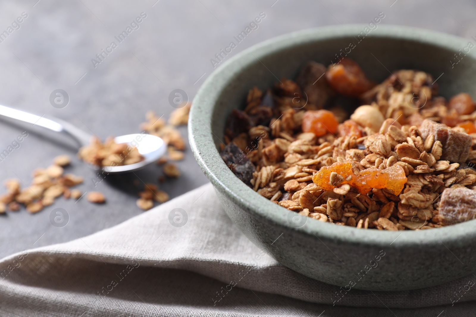 Photo of Tasty granola in bowl and napkin on gray table, closeup