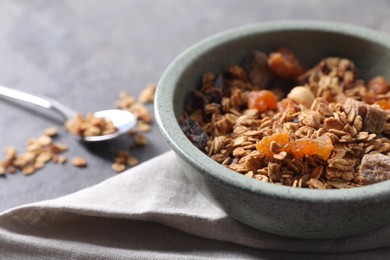 Photo of Tasty granola in bowl and napkin on gray table, closeup