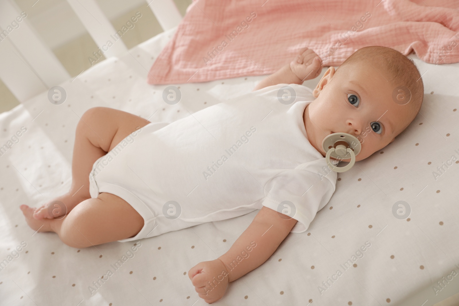 Photo of Cute little baby with pacifier lying in crib at home