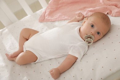 Cute little baby with pacifier lying in crib at home