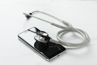 Photo of Modern smartphone and stethoscope on white table