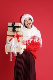 Woman in Santa hat, scarf and sweater holding Christmas gifts on red background