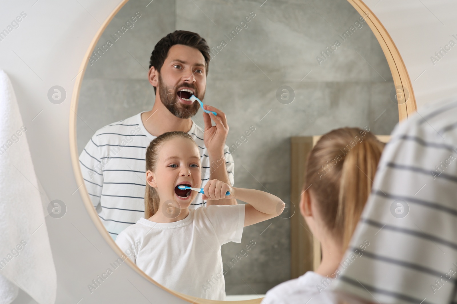 Photo of Father and his daughter brushing teeth together near mirror in bathroom