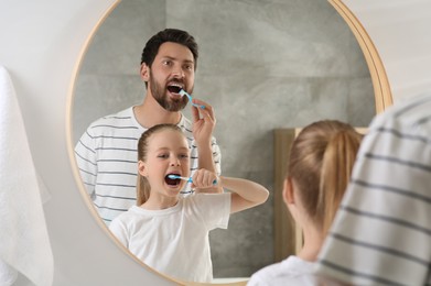 Father and his daughter brushing teeth together near mirror in bathroom