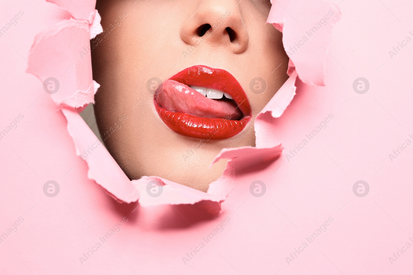 Photo of View of beautiful young woman with red lips through hole in color paper, closeup