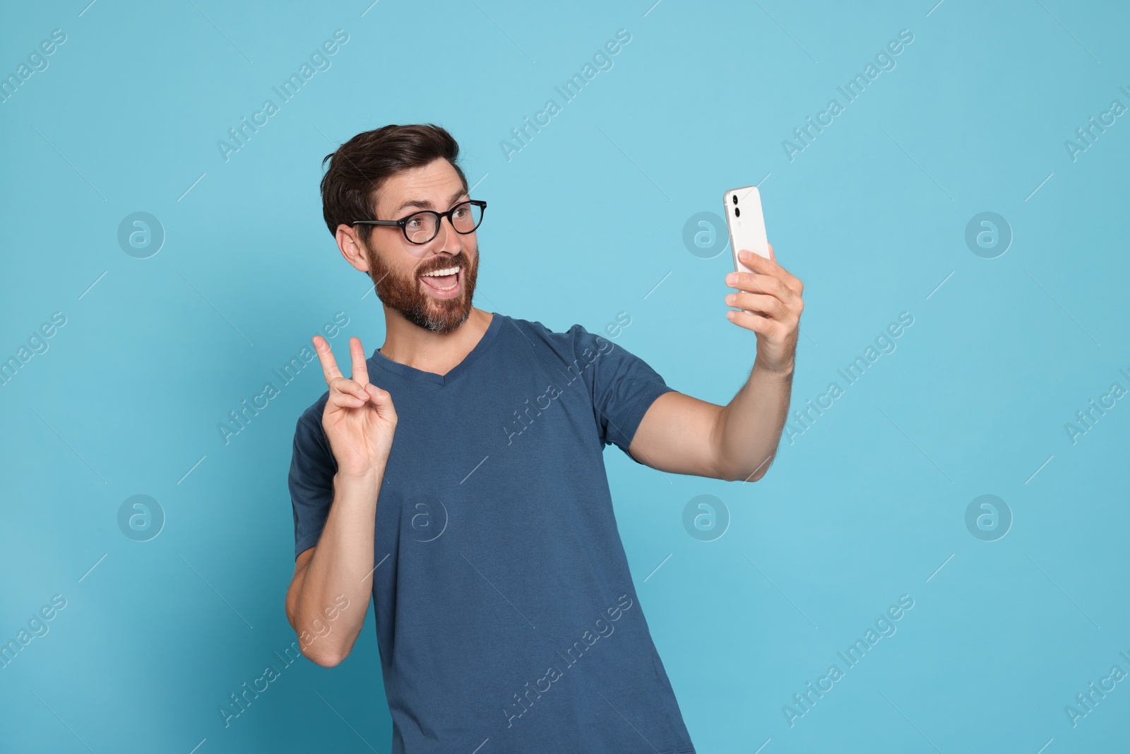 Photo of Happy man taking selfie with smartphone on light blue background