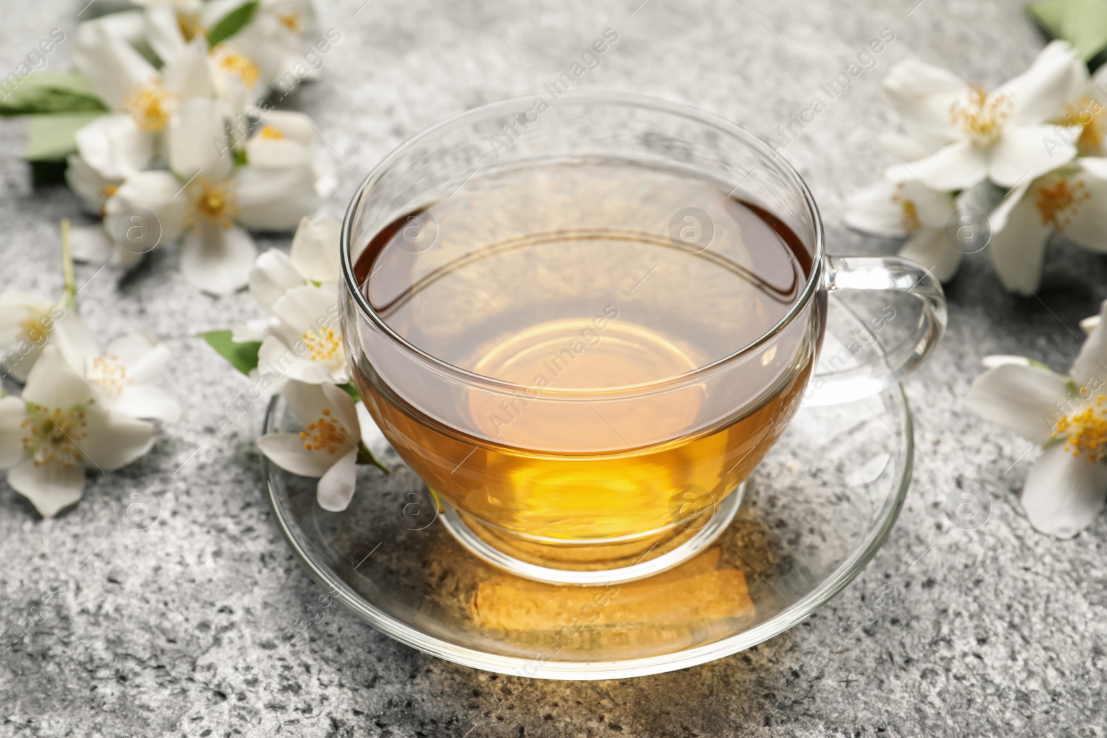 Photo of Glass cup of aromatic jasmine tea and fresh flowers on grey table
