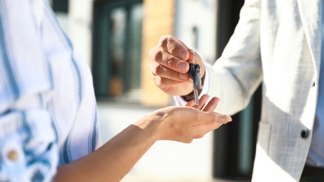 Photo of Real estate agent giving house keys to young woman outdoors, closeup