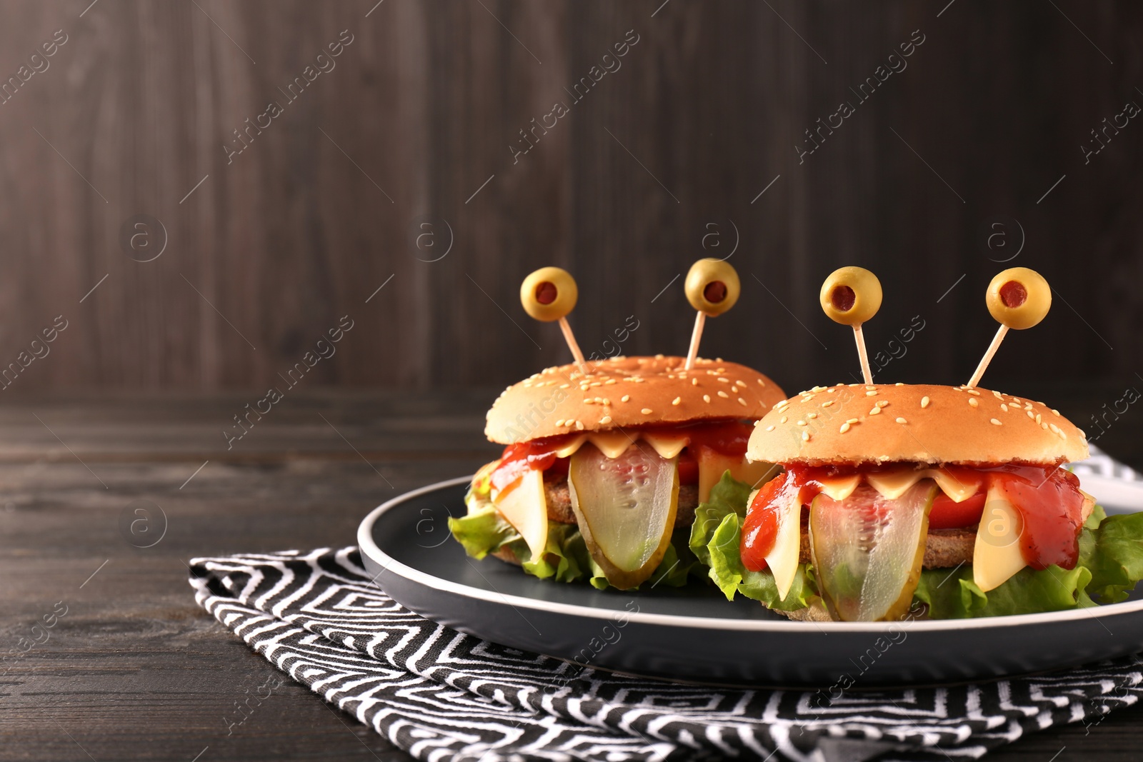 Photo of Cute monster burgers on wooden table, space for text. Halloween party food