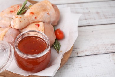 Fresh marinade, raw chicken drumsticks, rosemary and tomato on white wooden table, closeup. Space for text