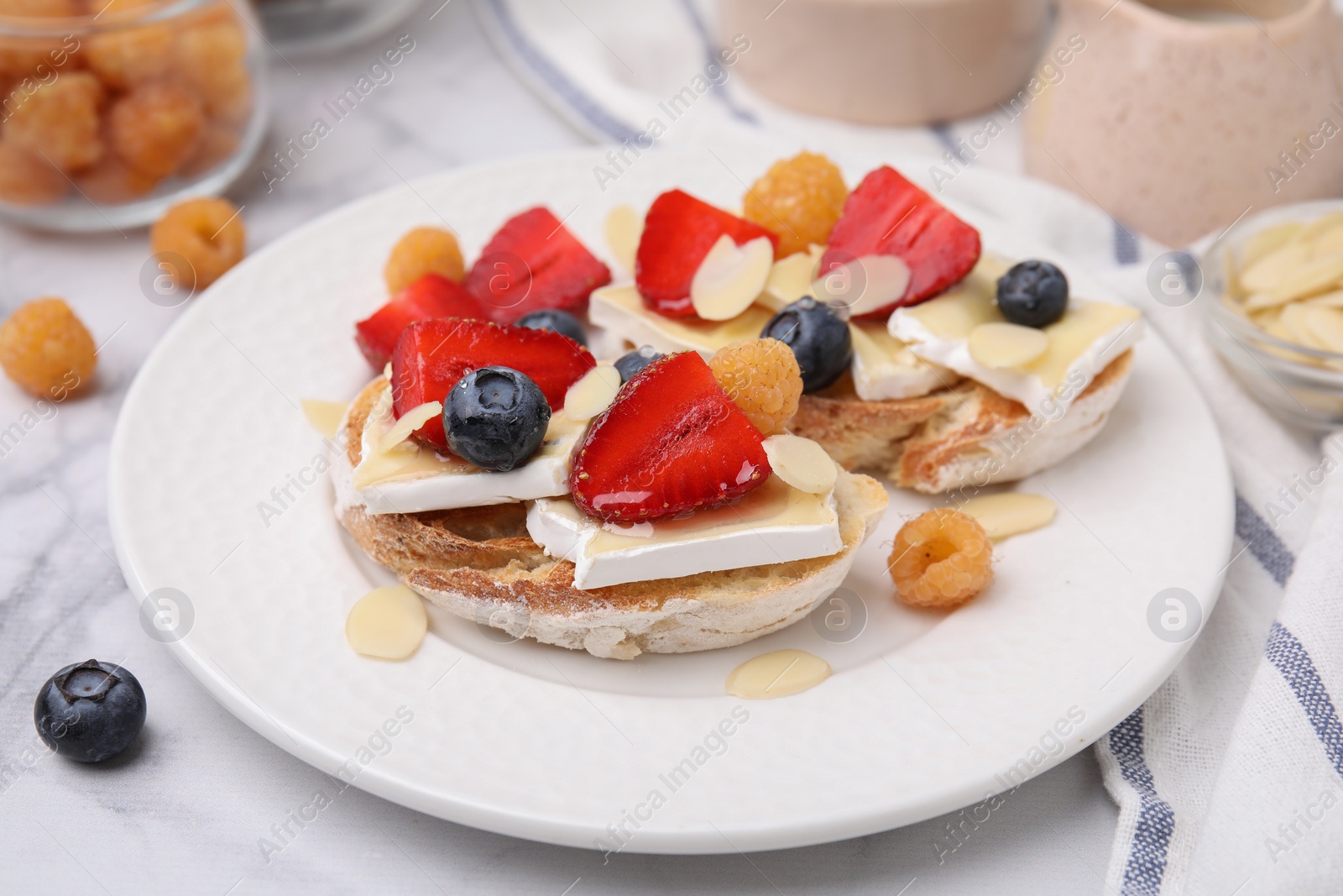 Photo of Tasty sandwiches with brie cheese, fresh berries and almond flakes on white marble table, closeup