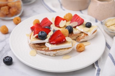 Photo of Tasty sandwiches with brie cheese, fresh berries and almond flakes on white marble table, closeup