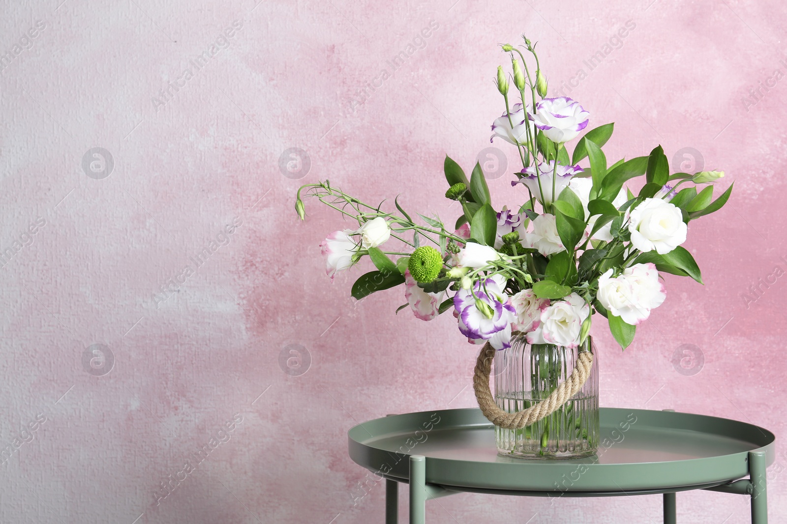 Photo of Vase with bouquet of beautiful flowers on table against color background. Space for text