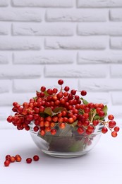 Photo of Bowl with ripe red viburnum berries on white wooden table