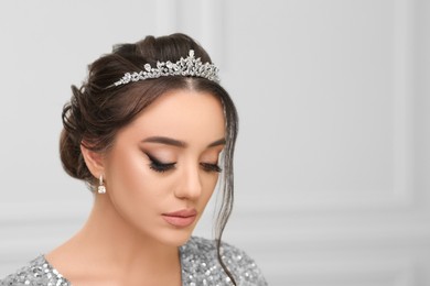Beautiful young woman wearing luxurious tiara indoors, space for text