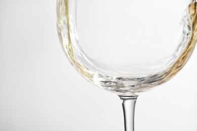 Pouring white wine into glass on light background, closeup