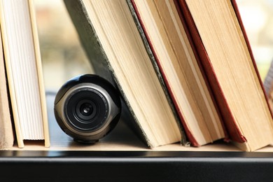 Photo of Camera hidden between books on wooden shelf indoors, closeup