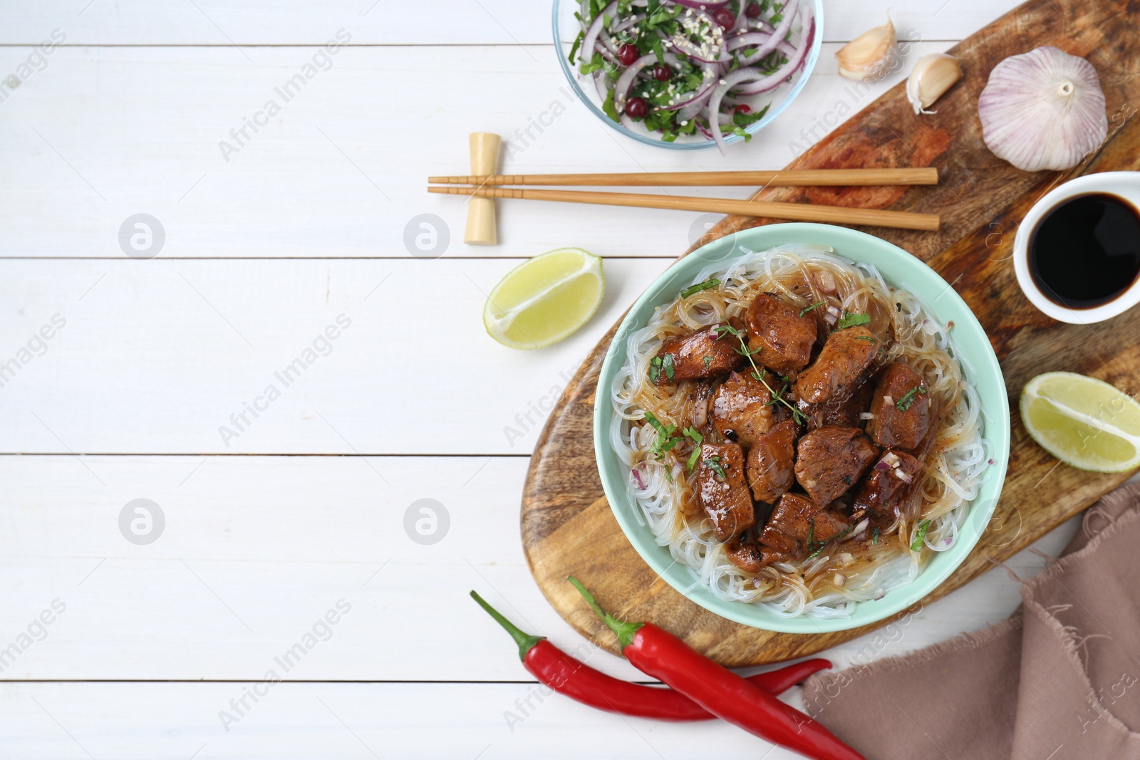 Photo of Bowl with pieces of soy sauce chicken and noodle on white wooden table, flat lay