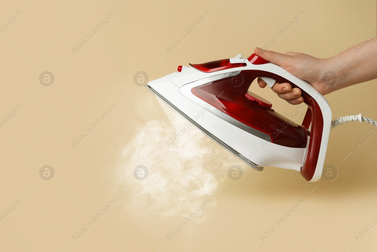 Image of Woman holding modern iron with steam on beige background, closeup