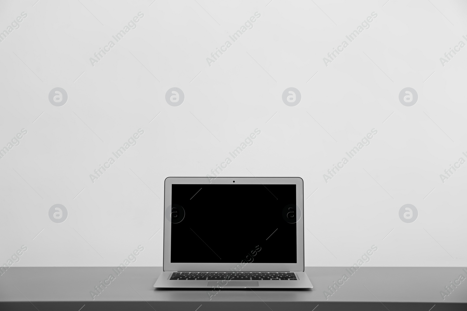 Photo of Modern laptop with blank screen on table against light background