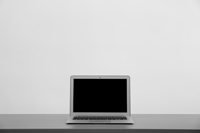 Photo of Modern laptop with blank screen on table against light background