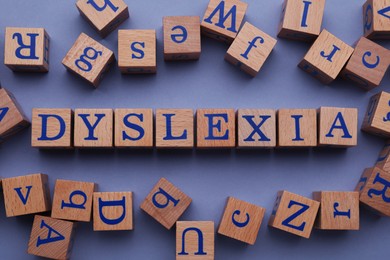 Photo of Wooden cubes with word Dyslexia on violet background, flat lay