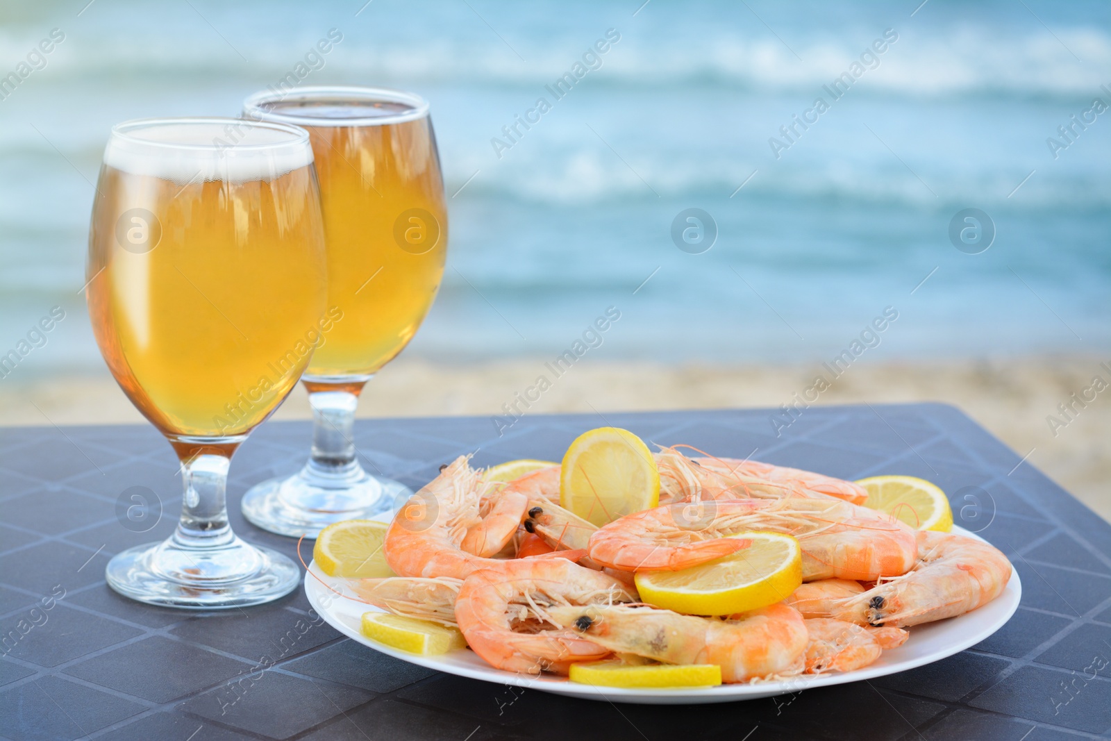 Photo of Cold beer in glasses and shrimps served with lemon on beach