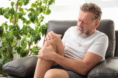 Senior man suffering from knee pain indoors