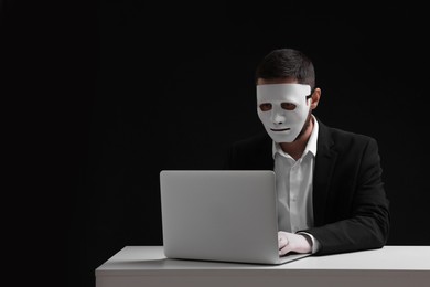 Photo of Man in mask and gloves working with laptop against black background. Space for text