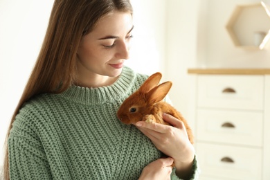 Photo of Young woman with adorable rabbit indoors. Lovely pet