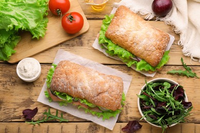 Delicious sandwiches with fresh vegetables and salmon on wooden table, flat lay