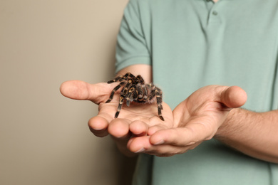 Photo of Man holding striped knee tarantula on beige background, closeup