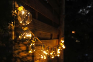 Photo of Garland of lamp bulbs hanging on wooden wall, space for text. String lights