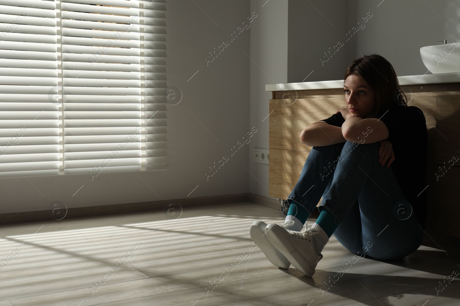 Photo of Sad young woman sitting on floor in bathroom, space for text