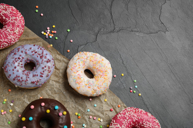 Photo of Yummy donuts with sprinkles on dark background, flat lay. Space for text