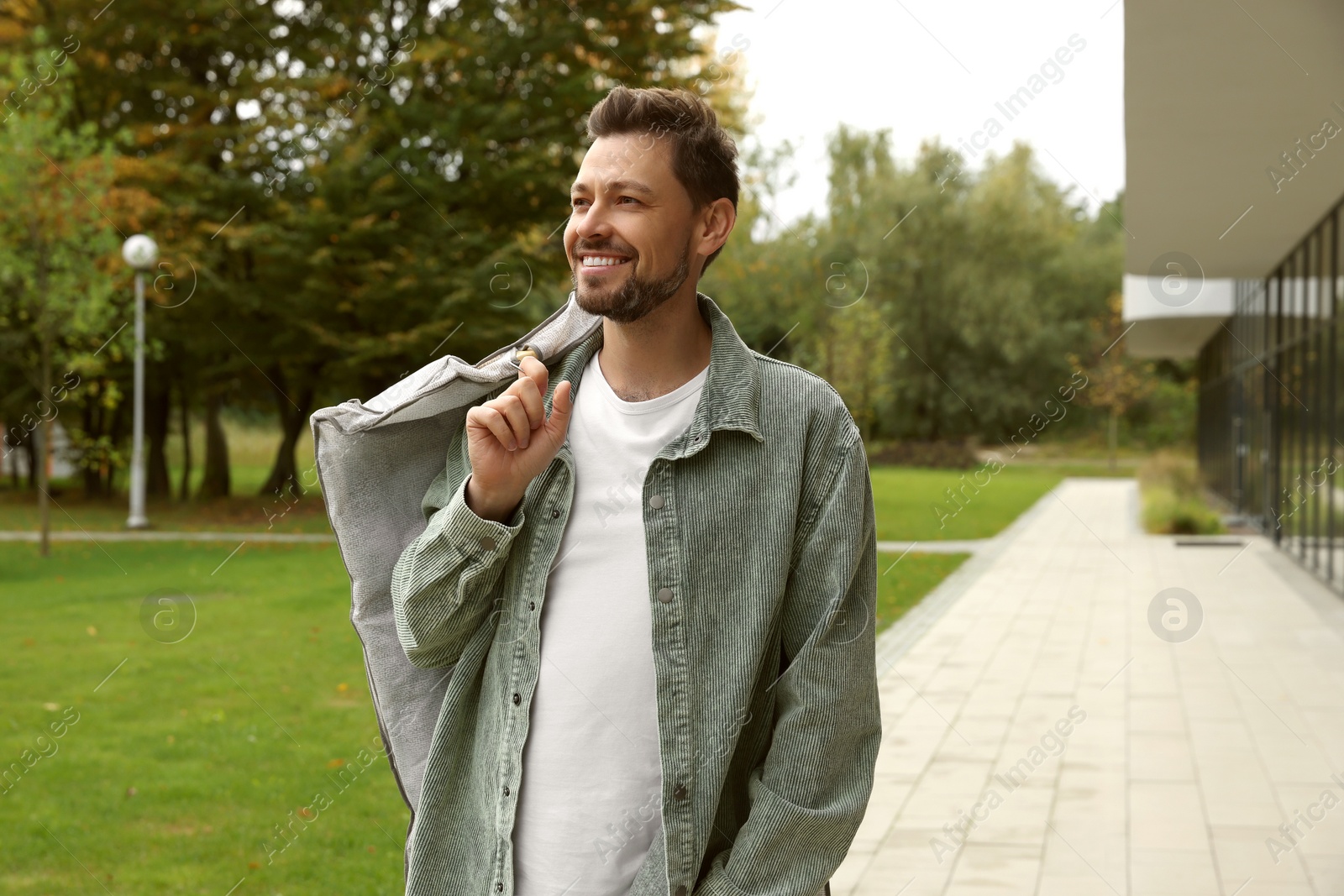 Photo of Attractive happy man holding garment cover with clothes outdoors. Dry cleaning service