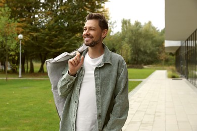 Attractive happy man holding garment cover with clothes outdoors. Dry cleaning service